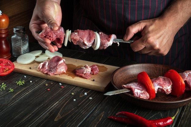 Lo chef professionista punge la carne cruda su uno spiedino Il processo di cottura dello shish kebab di carne