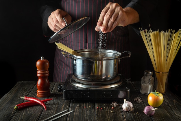 Lo chef sala la pasta biologica in una pentola calda in cucina Deliziosa ricetta del cibo dell'hotel Cucina tradizionale italiana