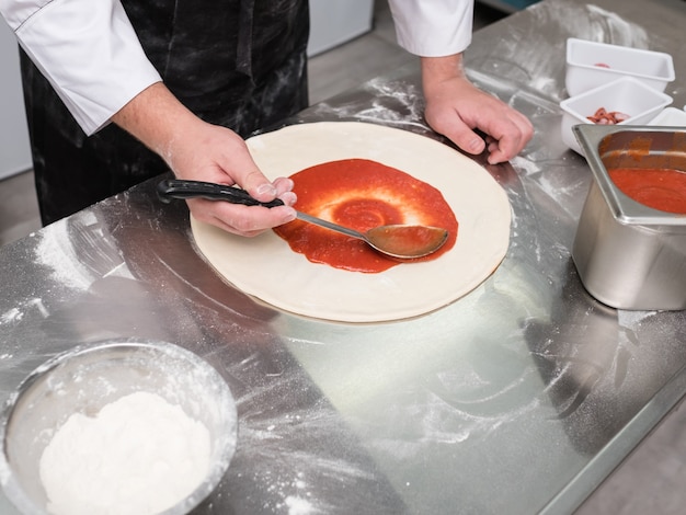 Lo chef spalma la salsa di pomodoro per pizza su un impasto seguendo una ricetta tradizionale italiana.