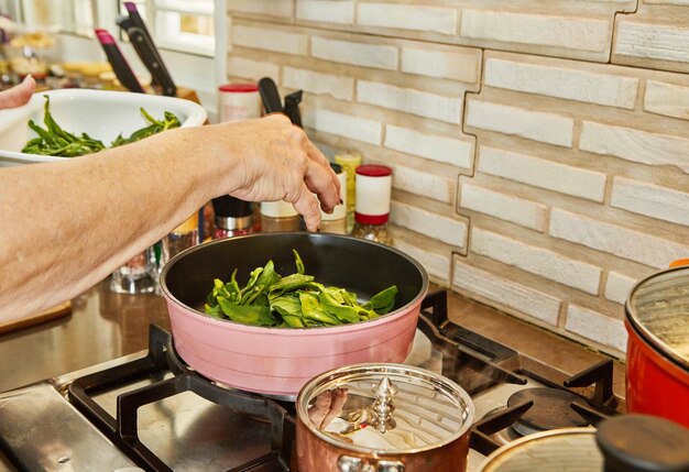 Lo chef sta friggendo l'acetosa in padella nell'olio sul fornello a gas