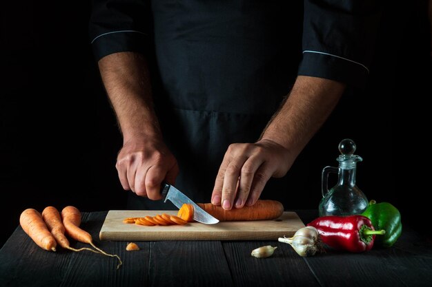 Lo chef sta tagliando le carote per la zuppa di verdure nella cucina del ristorante