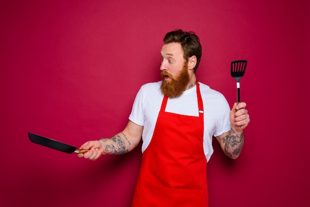 Lo chef stupito con barba e grembiule rosso è pronto per cucinare