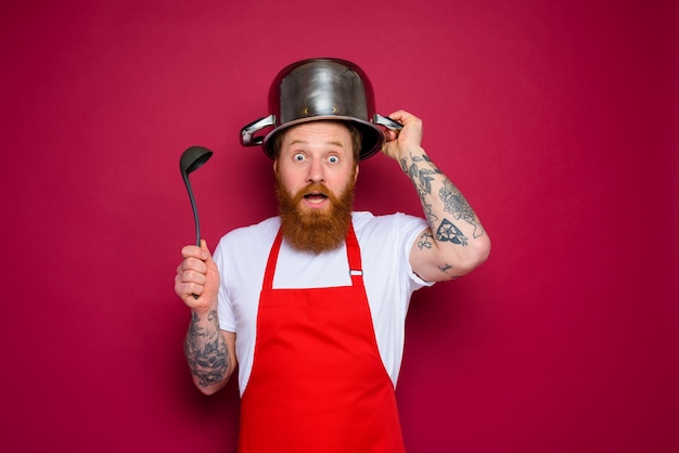 Lo chef stupito con barba e grembiule rosso gioca con la pentola