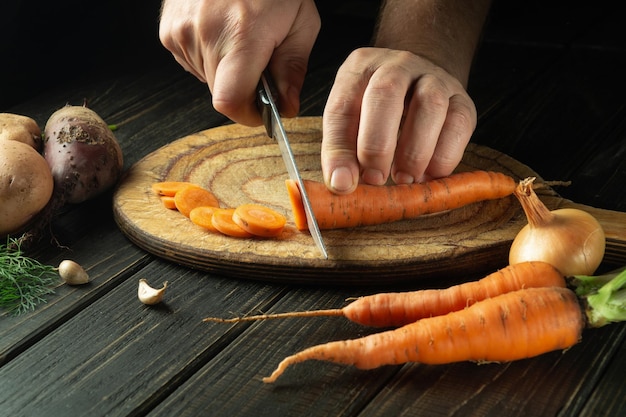 Lo chef taglia carote fresche su un tagliere di legno