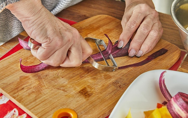 Lo chef taglia fette di carote di tre colori in cucina su tavola di legno