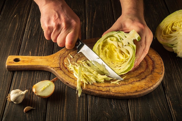 Lo chef taglia il cavolo con un coltello Cucinare insalata di verdure in un tagliere Alimenti contadini