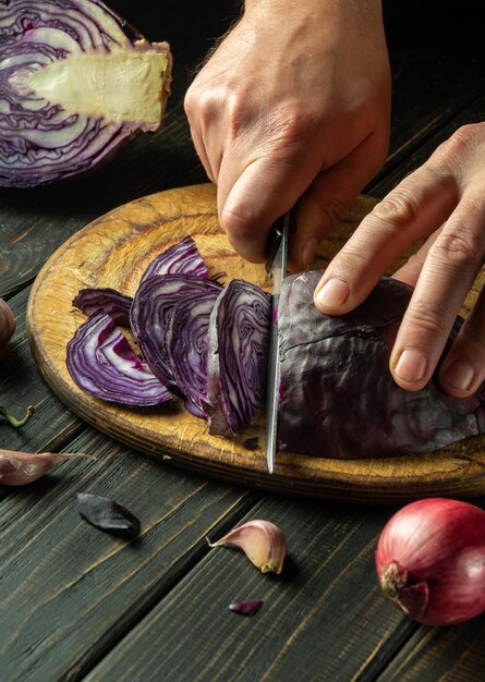 Lo chef taglia il cavolo rosso con un coltello Cucinare insalata di verdure nella cucina del ristorante Idea di dieta vegetale