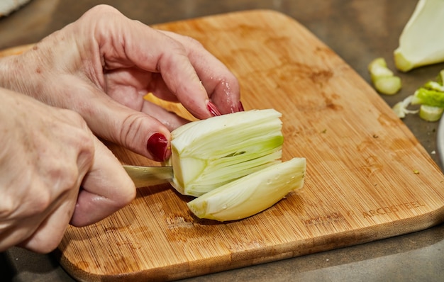 Lo chef taglia il finocchio secondo la ricetta di cottura su tavola di legno in cucina.