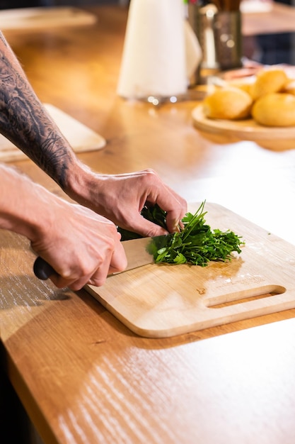 Lo chef taglia il prezzemolo con un coltello su una tavola di legno da vicino