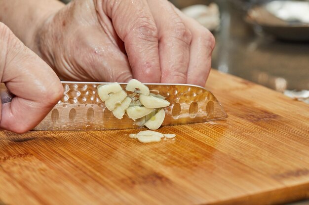 Lo chef taglia l'aglio su una tavola di legno in cucina