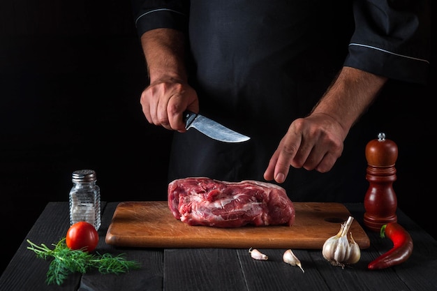 Lo chef taglia la carne con un coltello in cucina prepara il cibo Verdure e spezie sul tavolo della cucina in un ristorante per preparare un delizioso pranzo