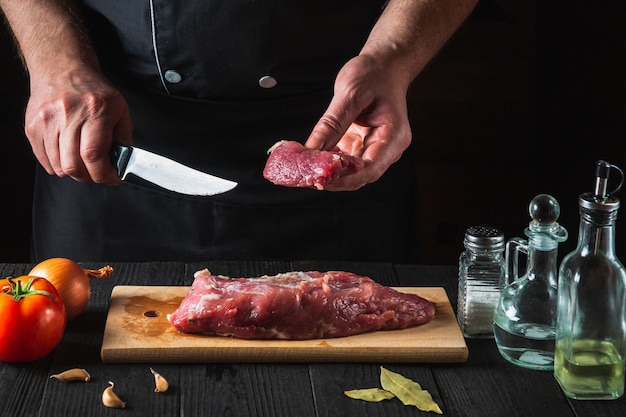 Lo chef taglia la carne di manzo con il coltello in cucina, cucinando il cibo. Verdure e spezie sul tavolo della cucina per preparare deliziosi pranzi