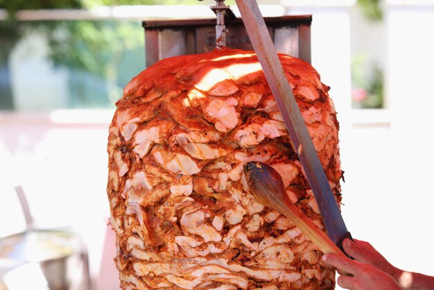 Lo chef taglia la carne di pollo alla griglia dallo spiedo rotante e prepara il tradizionale street food da strada