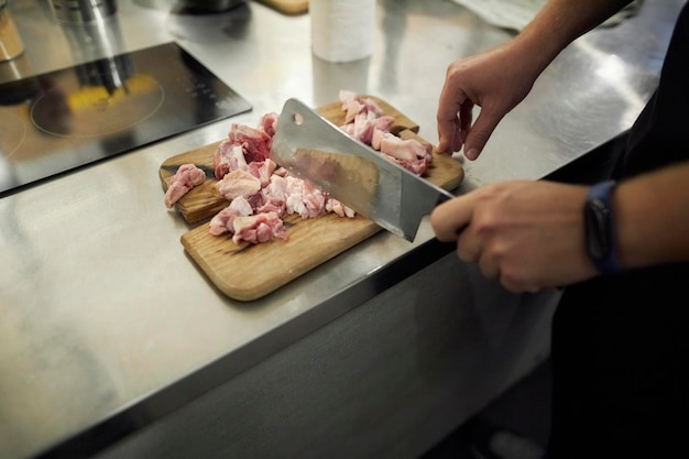 lo chef taglia la carne di pollo con un'ascia da cucina. le mani tagliano a pezzi la carne di pollo.