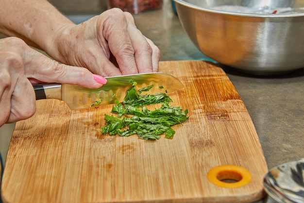 Lo chef taglia le foglie di basilico sul tagliere di legno con un coltello da aggiungere al piatto