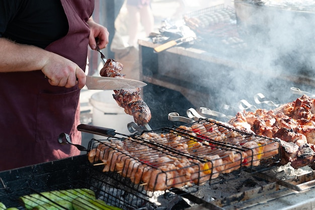 Lo chef taglia una carne alla griglia alla griglia in un ristorante di strada con un coltello Cibo di strada