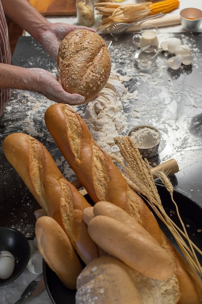 Lo chef tiene in mano il pane fresco. Uomo che prepara i panini al tavolo in cucina.