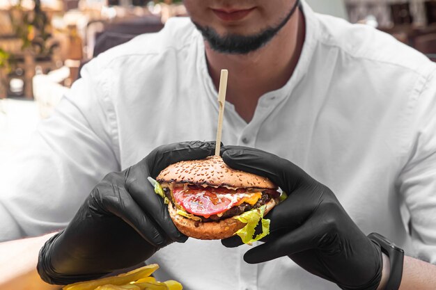 Lo chef tiene in mano un hamburger in guanti neri.