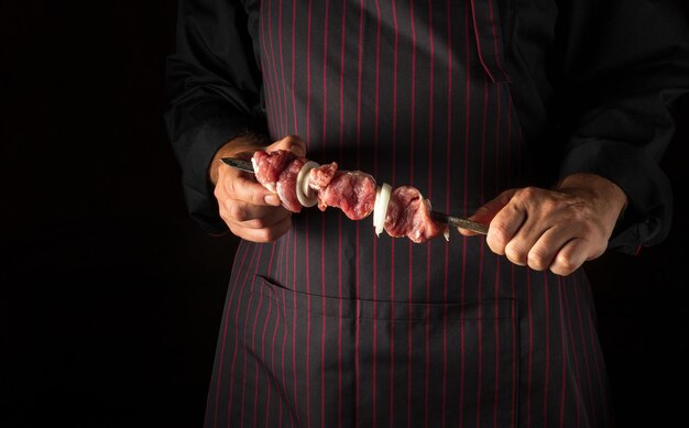 Lo chef tiene in mano uno shish kebab con carne di agnello cruda e cipolle su uno spiedino