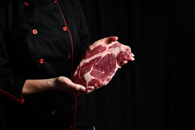 Lo chef tiene una bistecca di manzo ribeye, una bistecca invecchiata e maturata, carne su uno sfondo nero.