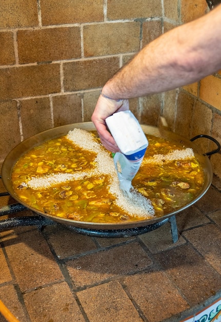 Lo chef versa il riso nella paella dopo aver cucinato i primi ingredienti per un'autentica paella valenciana