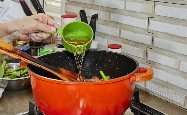 Lo chef versa l'olio nella carne di manzo tagliata a dadini per la cottura su un fornello a gas