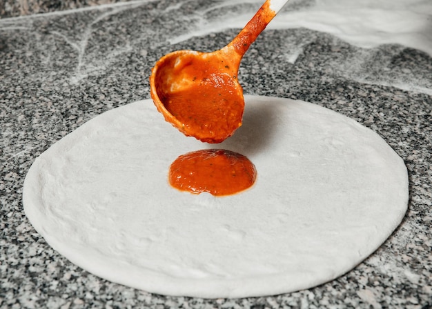 Lo chef versa la salsa di pomodoro sulla pasta arrotolata concetto ristorante cucchiaio da cucina il processo di preparazione della pizza italiana