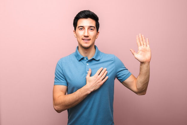 Lo giuro. bel giovane con un sorriso neutro in polo blu con la mano sul petto dando giuramento.