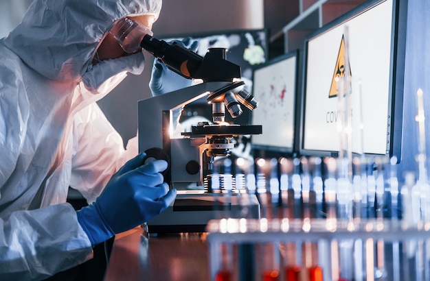 Lo scienziato in uniforme protettiva bianca lavora con coronavirus e provette di sangue in laboratorio