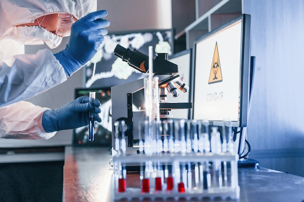 Lo scienziato in uniforme protettiva bianca lavora con coronavirus e provette di sangue in laboratorio