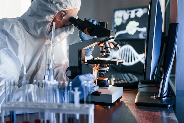 Lo scienziato in uniforme protettiva bianca lavora con coronavirus e provette di sangue in laboratorio