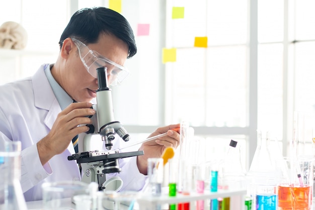 Lo scienziato maschio asiatico osserva tramite il microscopio in laboratorio.
