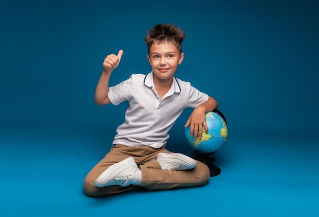 Lo scolaro allegro si siede su uno sfondo blu con uno zaino e un concetto di educazione del globo