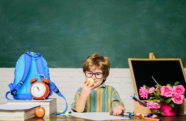 Lo scolaro del pranzo della scuola all'ora di pranzo Il ragazzino divertente con gli occhiali si siede alla scrivania in un bambino in classe