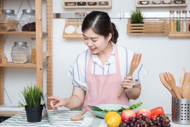 Lo scorrevole asiatico del dito di uso della giovane donna sullo schermo della compressa prepara gli ingredienti per cucinare