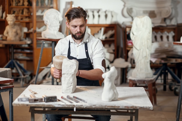 Lo scultore maschio in camicia bianca e grembiule nero fa una copia calcarea del torso di donna presso lo studio artistico.