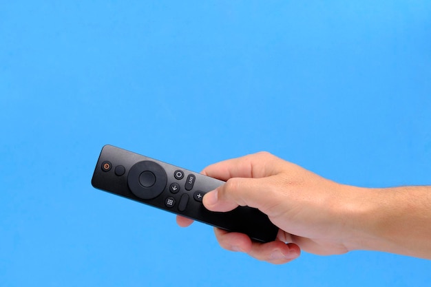 Lo sfondo blu della mano mantiene il telecomando della TV premendo il pulsante con il dito