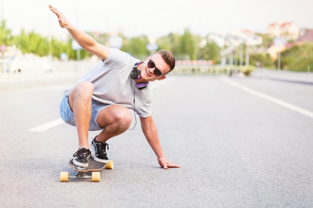 Lo skateboarder in occhiali da sole guida il longboard su strada asfaltata nel giro di trucco di posizione bassa della città