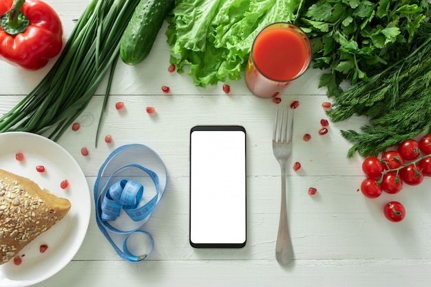 Lo smartphone si trova su un tavolo con verdure dietetiche. Posto per il tuo testo.