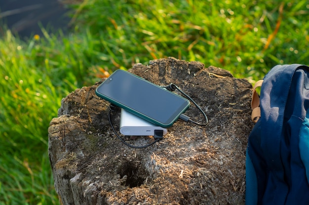 Lo smartphone viene caricato utilizzando un caricabatterie portatile. Power Bank ricarica il telefono all'aperto con uno zaino per il turismo nella natura.