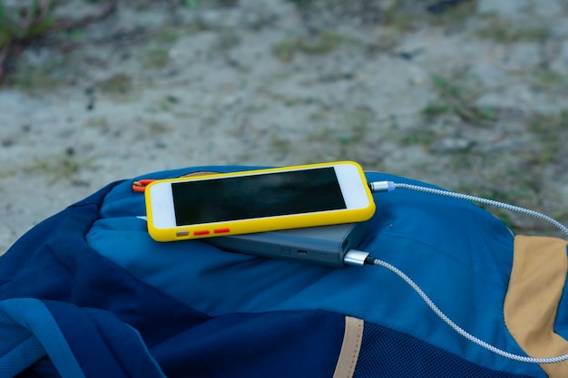 Lo smartphone viene caricato utilizzando un caricabatterie portatile. Power Bank ricarica il telefono all'aperto con uno zaino per il turismo nella natura.