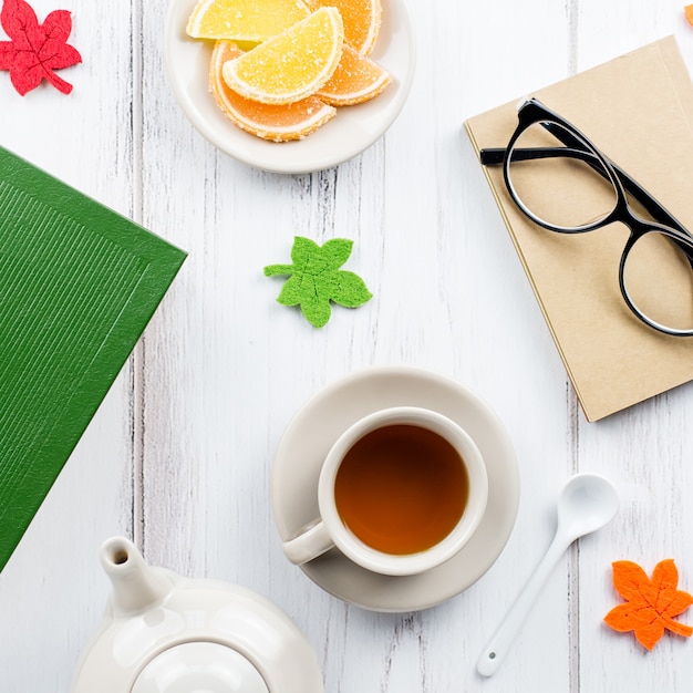 Lo spazio di lavoro femminile sulla scrivania è disteso con diario, occhiali, libro, tazza da tè, dolci e decorazioni in feltro.