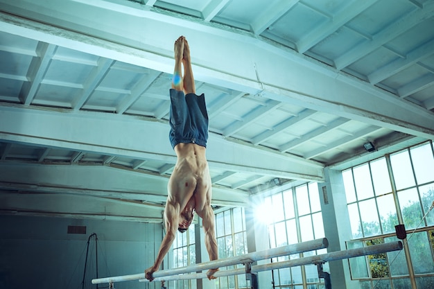 Lo sportivo che esegue un esercizio ginnico difficile in palestra. Lo sport, l'esercizio, la ginnasta, la salute, l'allenamento, il concetto di atleta. Modello in forma caucasica