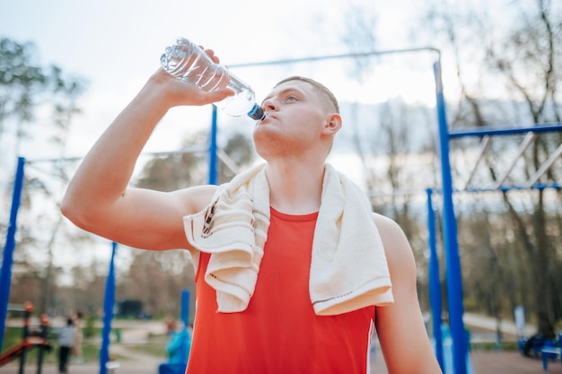 Lo sportivo maschio beve acqua durante l'allenamento all'aperto un tizio stanco fa una pausa dal suo s