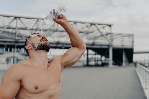 Lo sportivo stanco si rinfresca con pose di acqua dolce con il torso nudo all'aperto cerca di rinfrescarsi conduce uno stile di vita attivo si prende una pausa dopo l'allenamento cardio