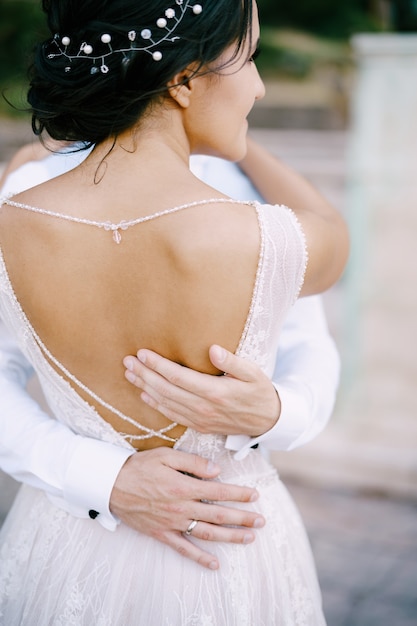 Lo sposo abbraccia dolcemente la sposa in un vestito elegante con le mani posteriori aperte dello sposo sulla vita di