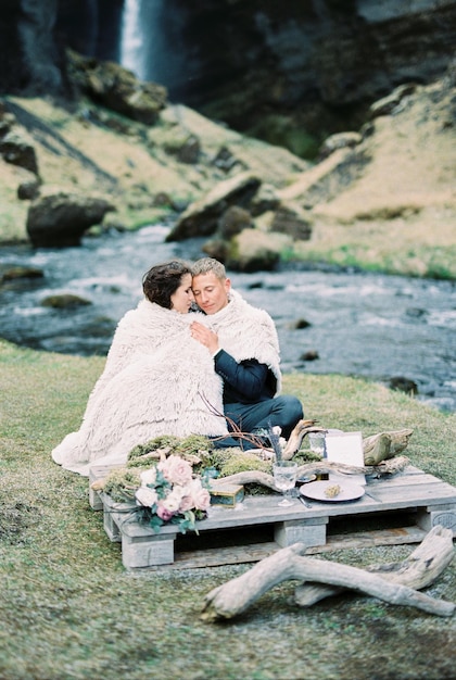 Lo sposo abbraccia la sposa nella coperta sulla riva del fiume alla tavola apparecchiata islanda