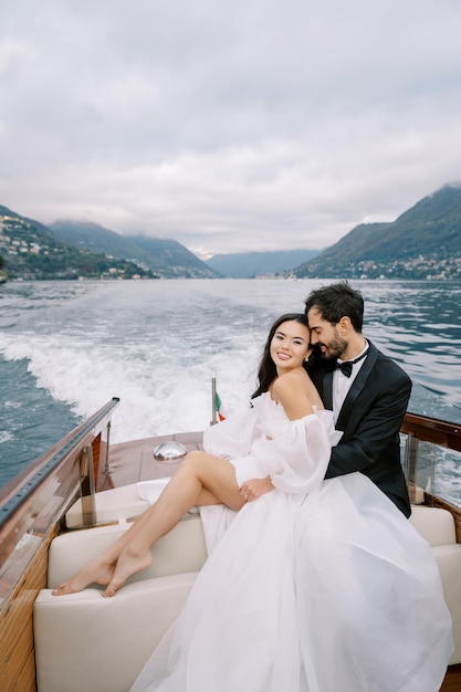 Lo sposo abbraccia la sposa sorridente da dietro su uno yacht che naviga sul lago Como in Italia