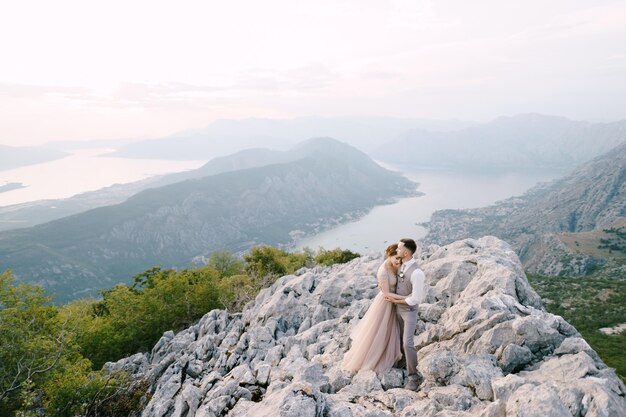 Lo sposo abbraccia la sposa sulla montagna sullo sfondo del drone della baia di Kotor