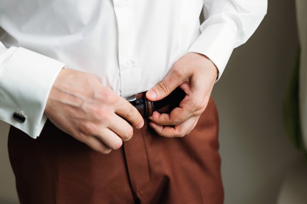 Lo sposo allaccia la cinghia sui pantaloni marroni